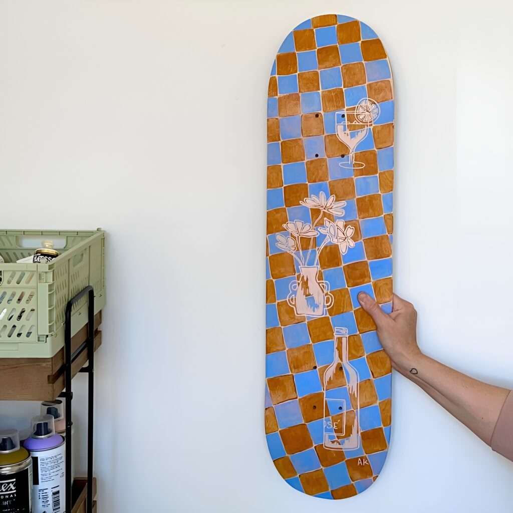 Skateboard wall art girly design with hand-painted checkered background and delicate floral and drink illustrations, adding charm to a creative bedroom space.