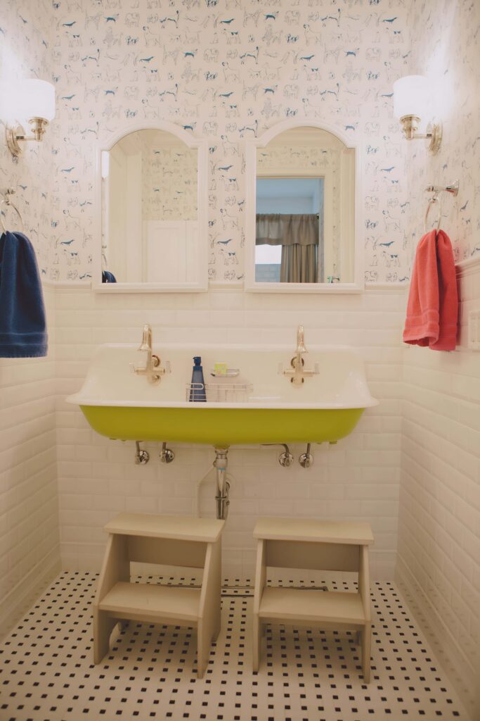 Charming kids bathroom design featuring a lime green double sink, playful animal wallpaper, dual mirrors, and step stools for easy access.