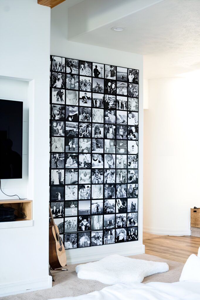 A large black and white aesthetic wall collage made up of multiple framed photos arranged in a grid pattern, displayed in a bright, modern living room corner with a guitar and cozy rug nearby.