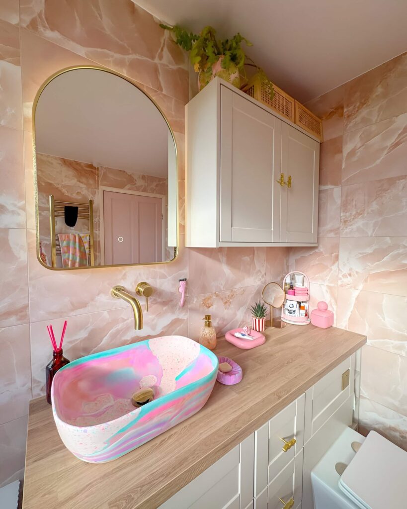 Colorful girls' bathroom design featuring a pink and teal swirl sink, gold fixtures, marble-effect tiles, and playful accessories on a wood countertop.