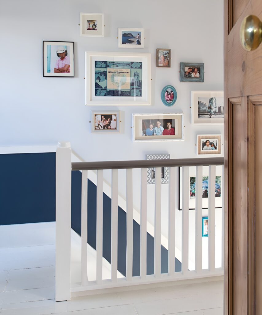 An eclectic staircase memory wall featuring a creative arrangement of family photos and keepsakes in mismatched frames on a white and navy accent wall.
