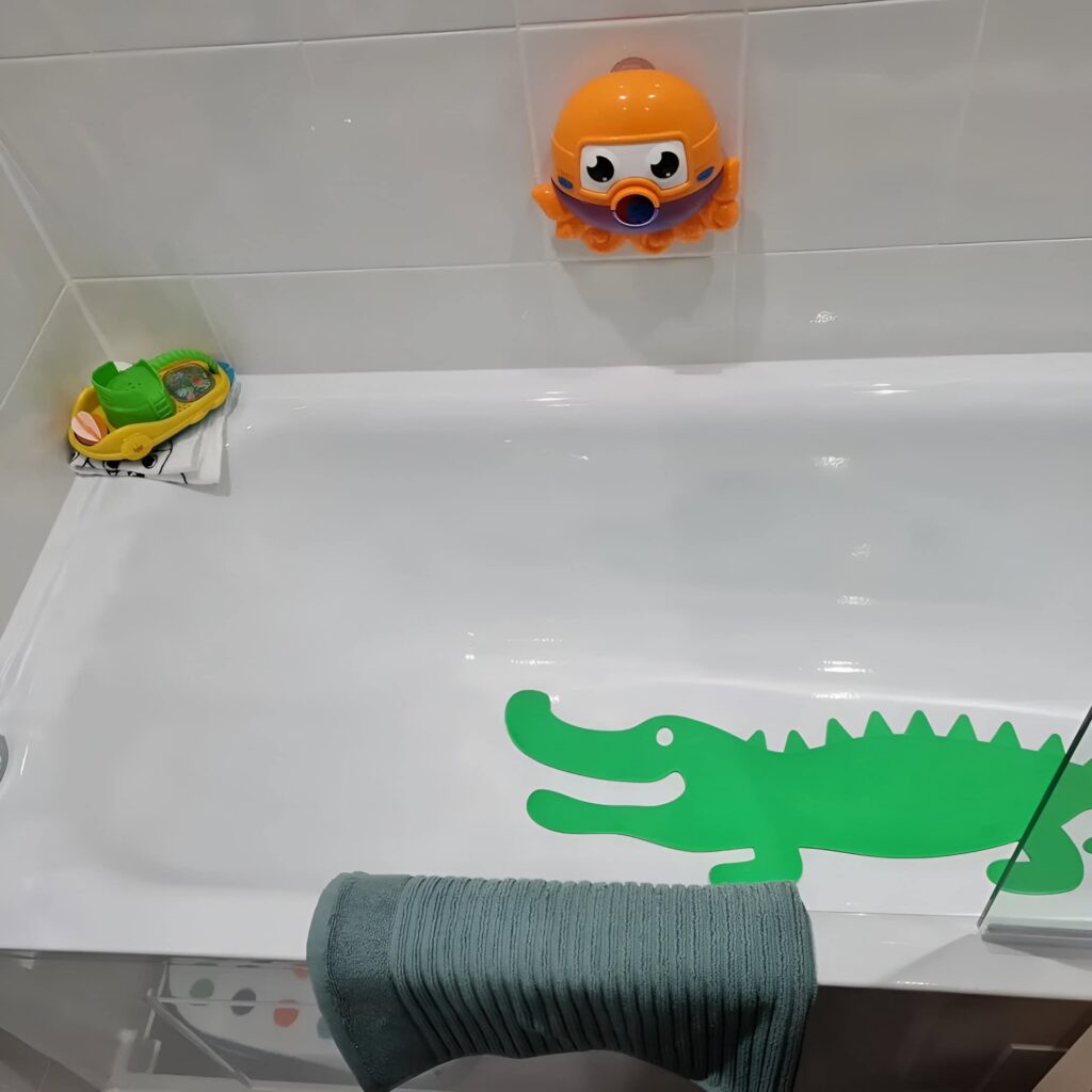 Playful boys' bathroom design featuring a white bathtub with a green crocodile decal, toy boat, and a bright orange wall-mounted octopus toy.