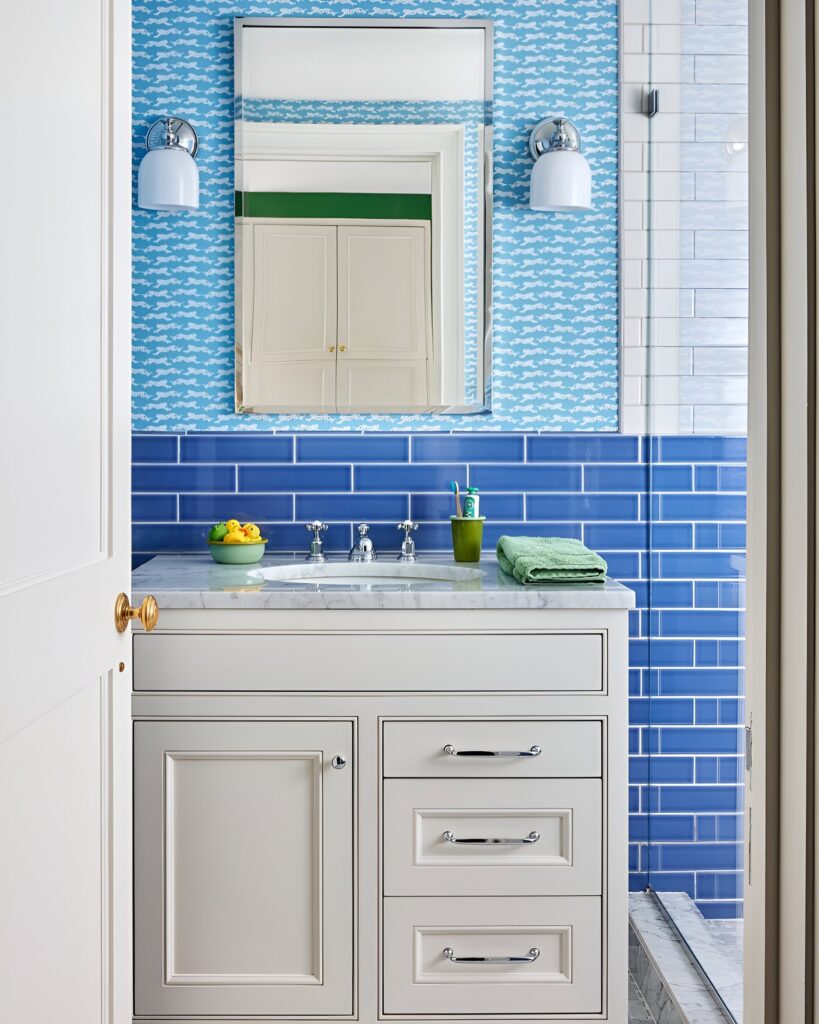 A fresh and bright bathroom featuring a blue tile backsplash, playful wallpaper, and marble vanity, offering modern bathroom design ideas for a boy’s space.