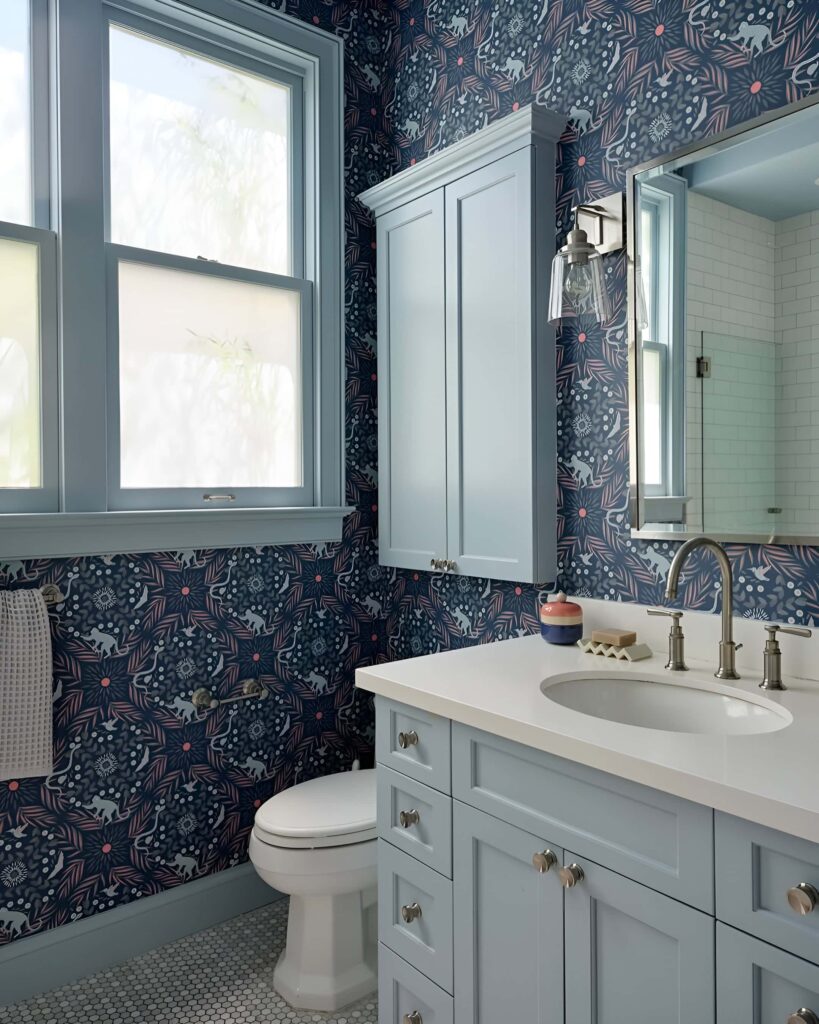 Stylish kids bathroom design with light blue cabinetry, playful patterned wallpaper, and modern bathroom decoration elements including brushed nickel fixtures and a clean white countertop.