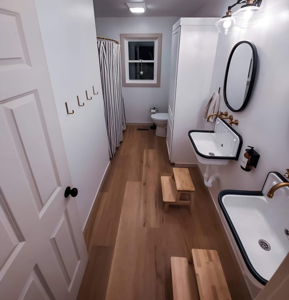 A modern and sleek bathroom design with dual sinks, wooden step stools, and minimalist decor, offering practical bathroom design ideas for a kid's space.