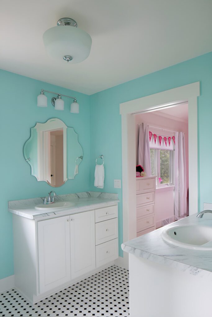 A bright and cheerful bathroom with teal walls, white cabinetry, and marble countertops, offering stylish bathroom design ideas for a kid's space.