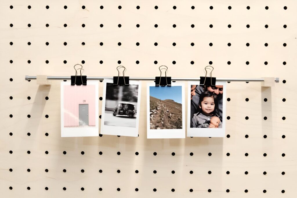 Pegboard photo display featuring four printed photographs clipped to a horizontal rod, creating a minimalist and modern wall art arrangement.