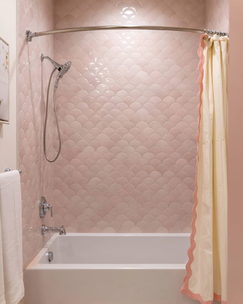 Chic girls' bathroom design featuring soft pink scallop tile walls, a curved shower curtain rod, and a white tub with a pastel-trimmed curtain.