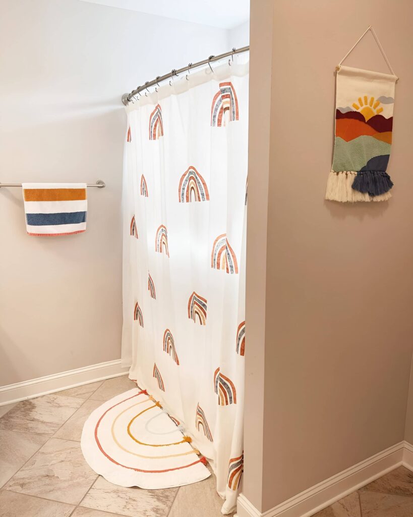 Playful bathroom design for girls featuring a rainbow-themed shower curtain, matching bath mat, striped towel, and colorful wall hanging in a bright, modern space.
