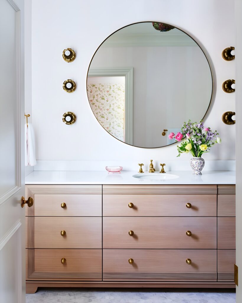 Chic and feminine kids bathroom design featuring a large round mirror, soft wood vanity with gold hardware, and floral accents for a timeless look.