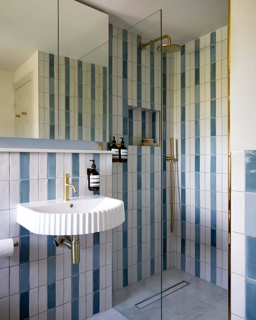 Playful vertical striped tile bathroom design with gold fixtures and a ribbed wall-mounted sink, perfect for a modern boys' bathroom.