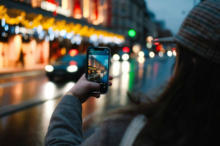 Person using a smartphone to photograph a vibrant, colorful city street at night, showcasing content for a city-themed Instagram page strategy.